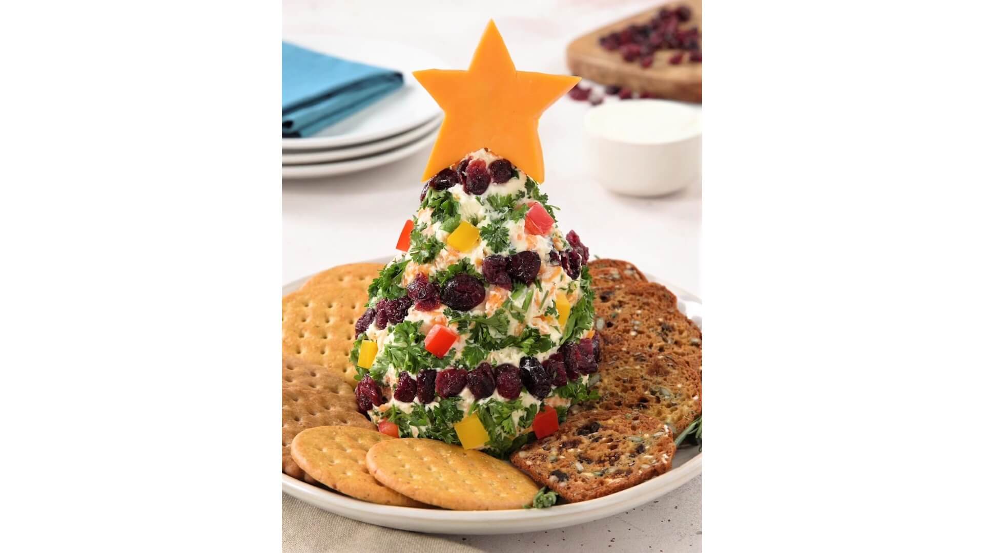 Plate holding a cheese ball shaped as a tree with garnishes displayed as ornaments. Topped with Cheddar cheese shaped as a star 