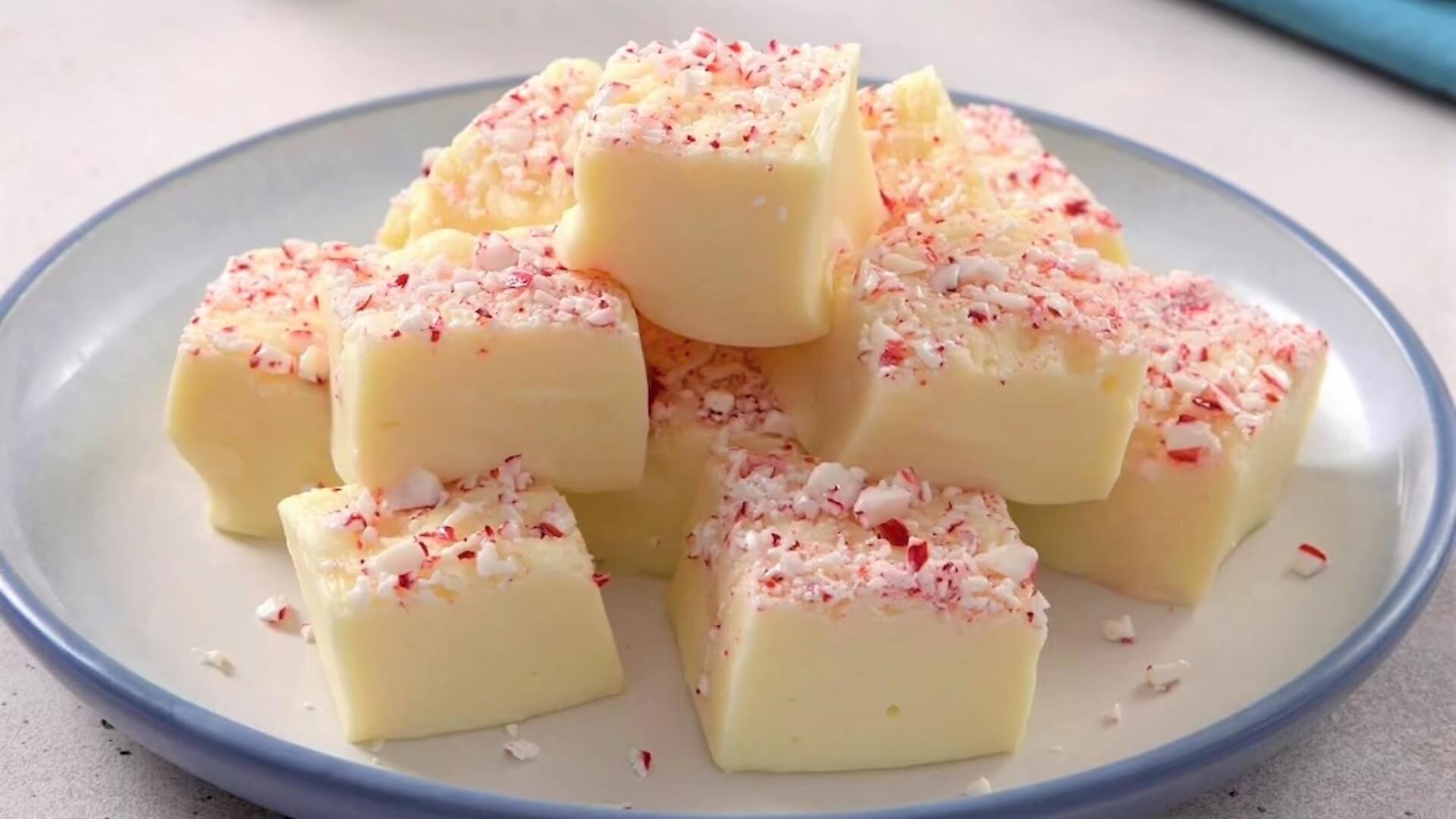 Plate of white fudge cut into squares and topped with crushed peppermint candy cane