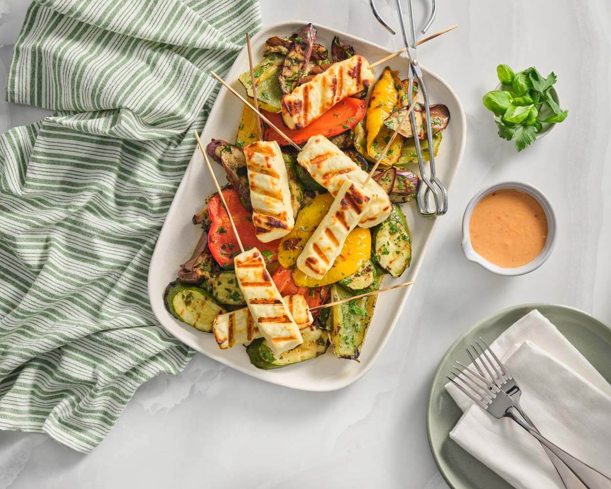 dish of salad on top of a green striped towel with grilled halloumi on skewers on a bed of vegetables