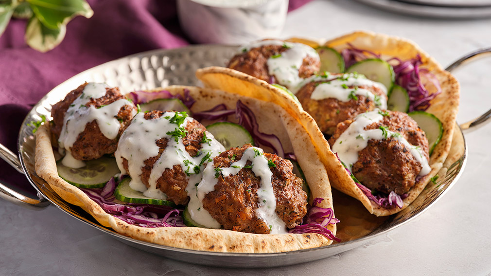Two Meatball Pitas with Buttermilk Herb Sauce sit on a hammered metal plate that sits on a white marble table.