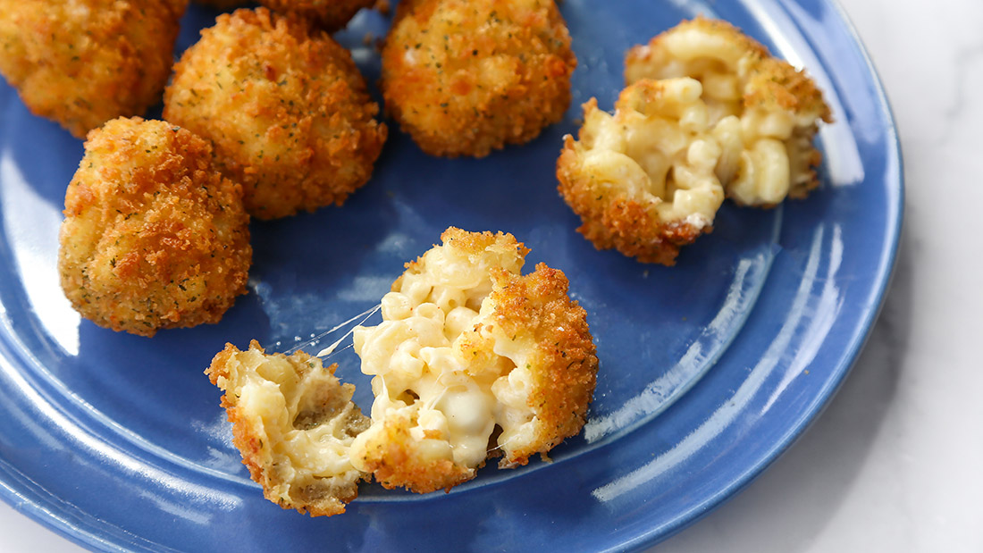Plate with multiple deep fried mac and cheese balls. Two broken open showing cheesy insides