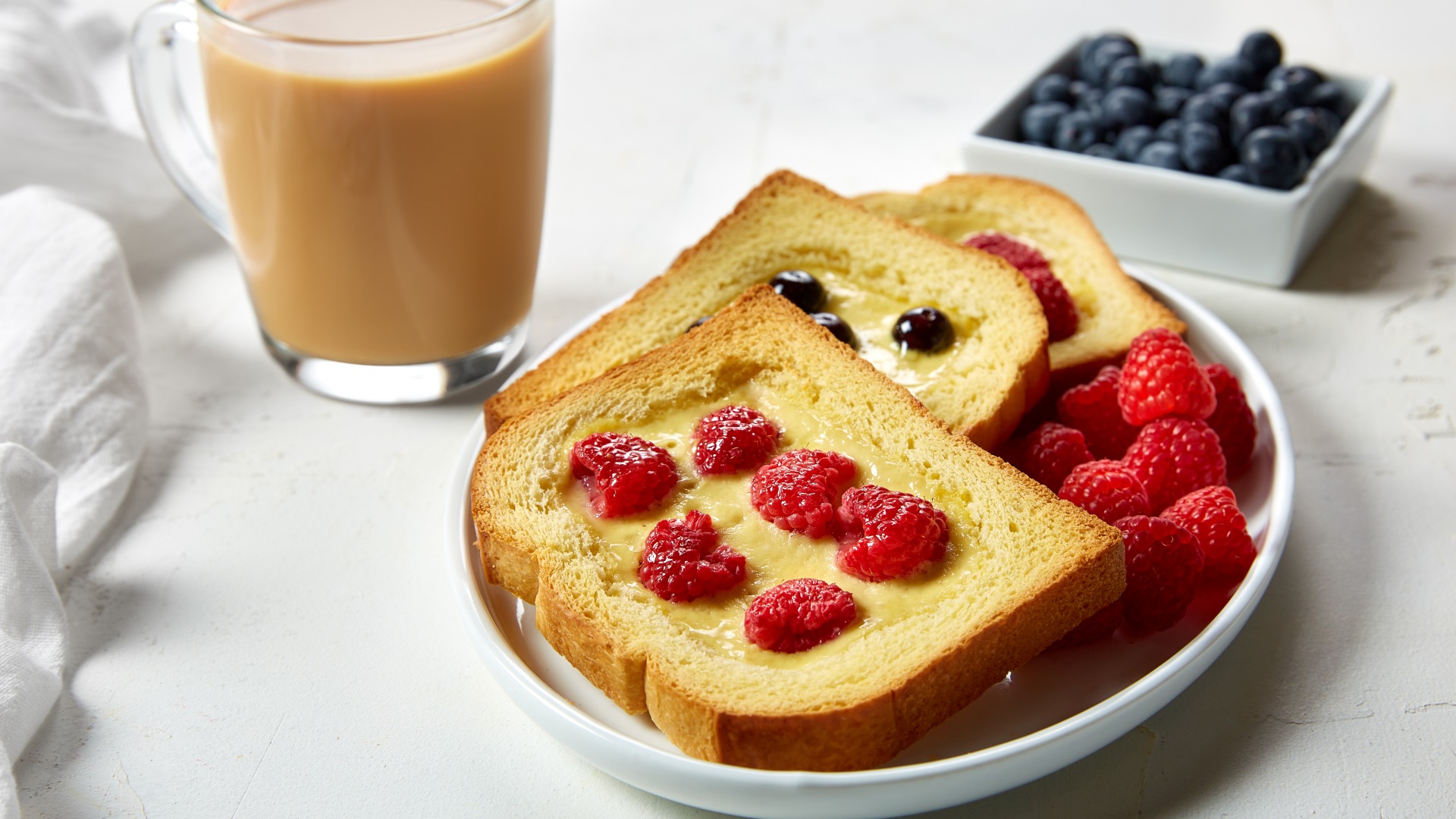 Plate with 3 pieces of toast with yogurt custard and fruit baked onto each slice. Glass of whitened coffee on the side