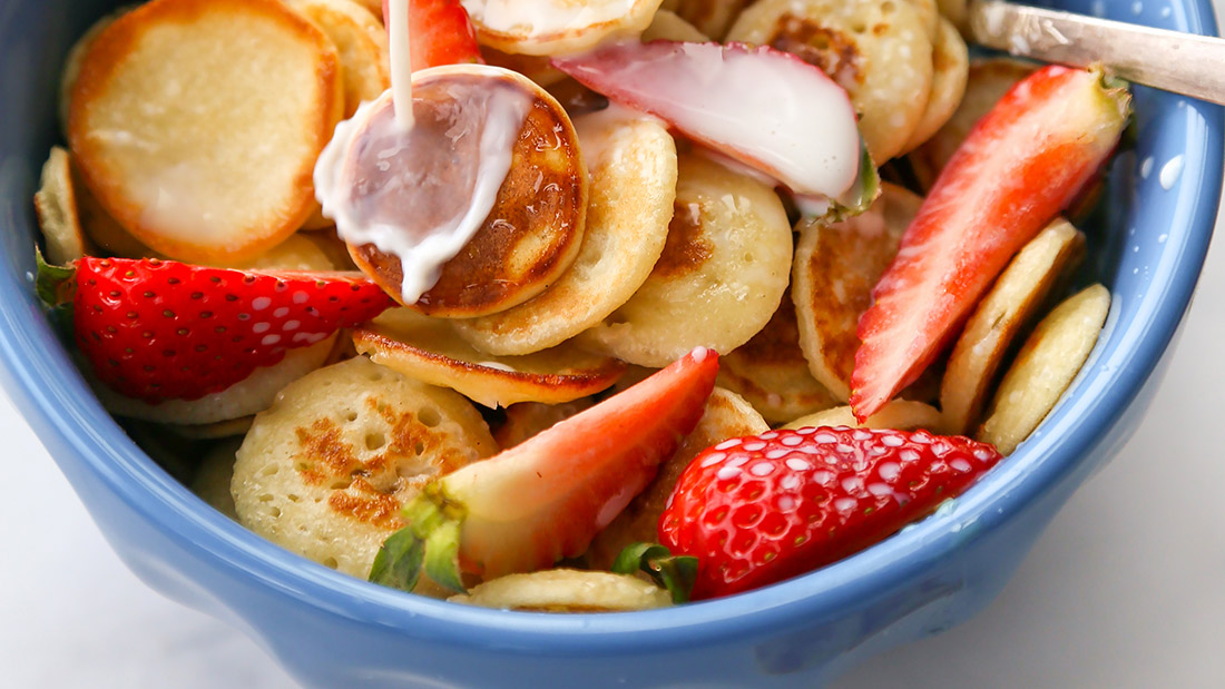 Cereal bowl with mini pancakes and cut strawberries.