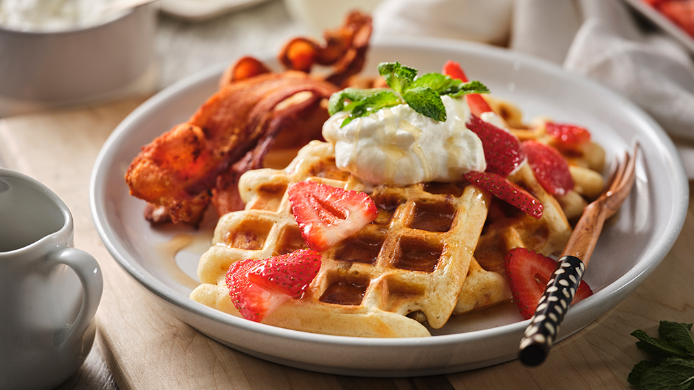 Buttermilk bacon waffles topped with bacon slices, dollop of whipped cream and strawberries.