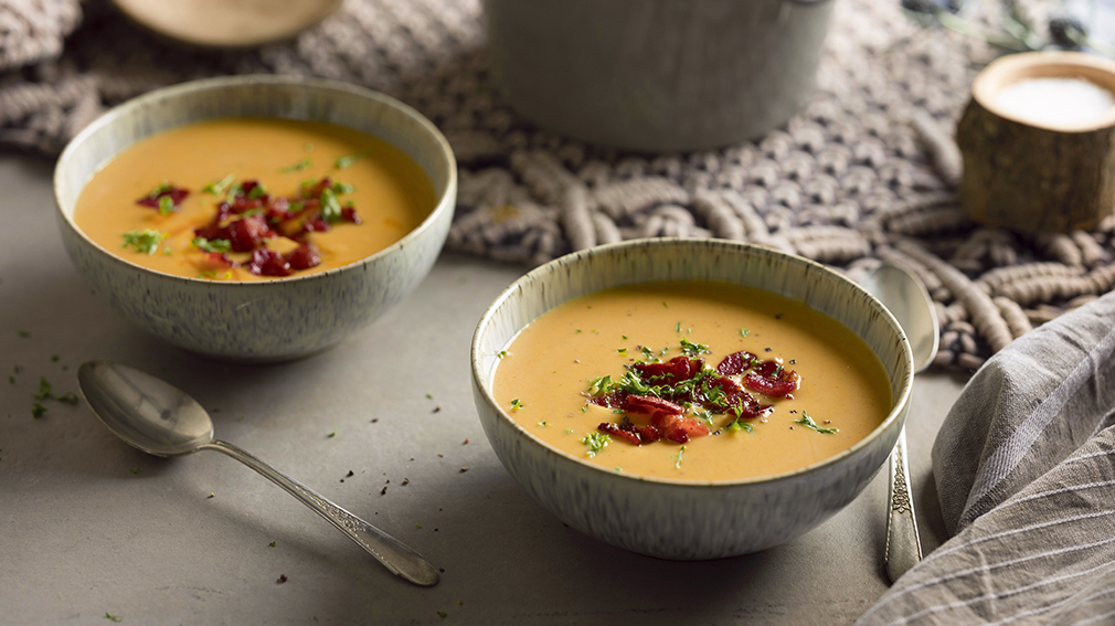 Sweet potato soup in small white bowl x2 with bacon and parsley garnish