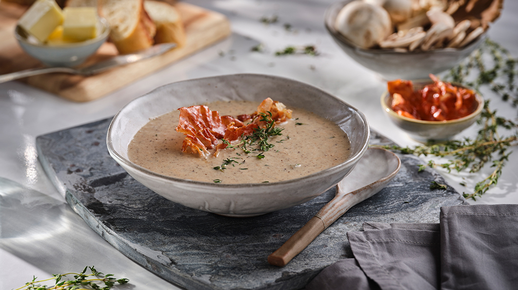 Mushroom soup in white bowl with bacon and thyme garnish