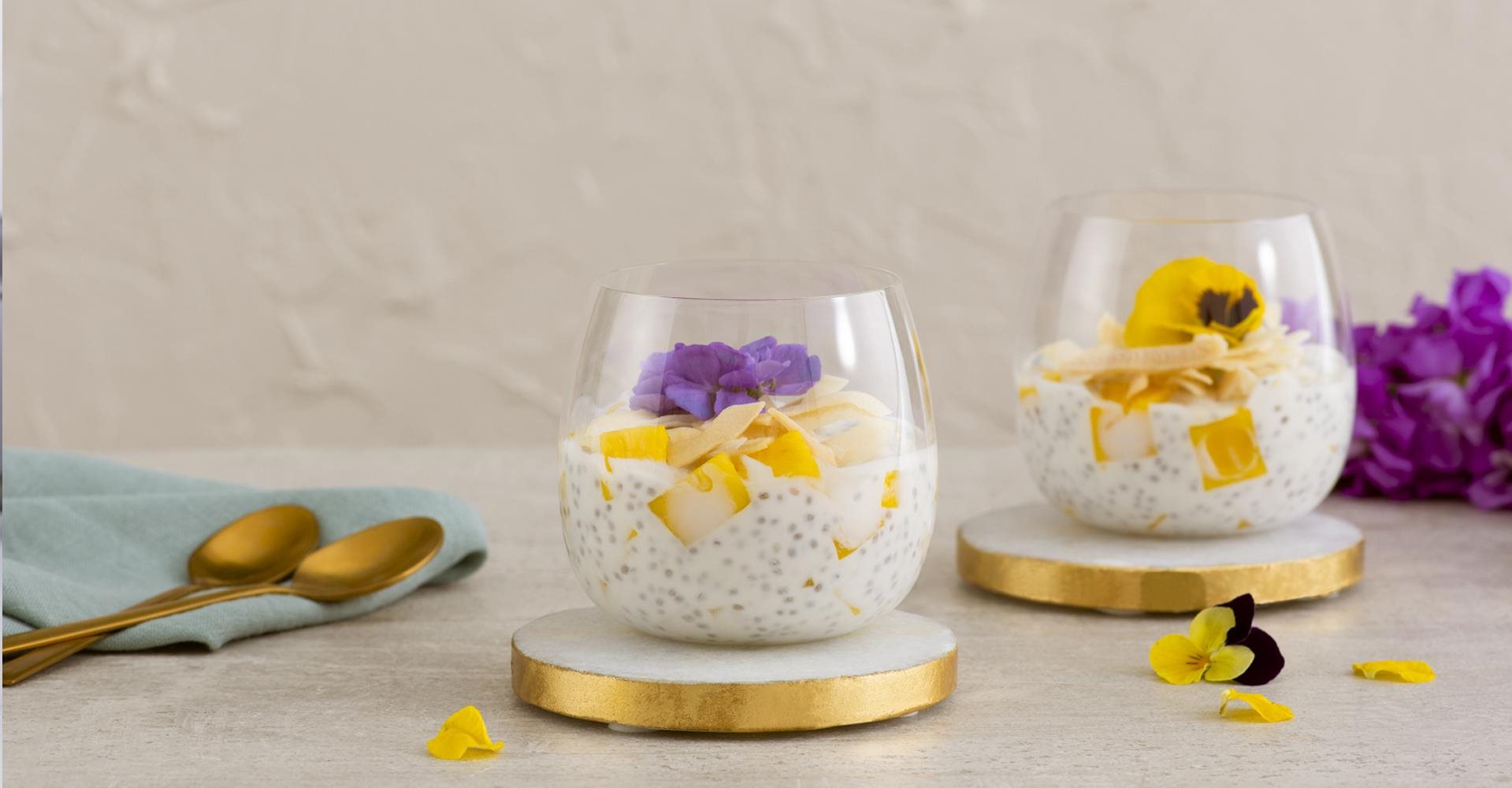 Mango Coconut Chia Pudding on table with flower pedals and gold spoons.