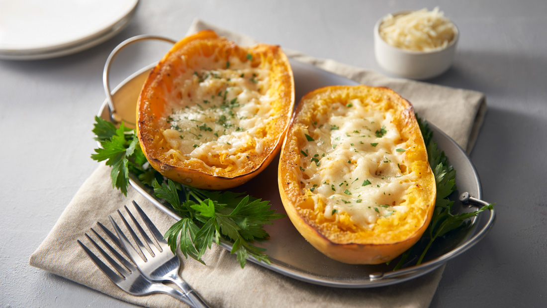 A long plate with two handles on each short side with two Cheesy Baked Spaghetti Squash halves garnished with fresh parsley