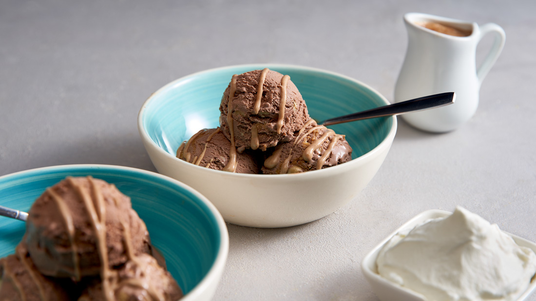 Two white and blue bowls each with three scoops of Chocolate Peanut Butter Ice Cream with an extra chocolate peanut butter drizzle over top of the ice cream.