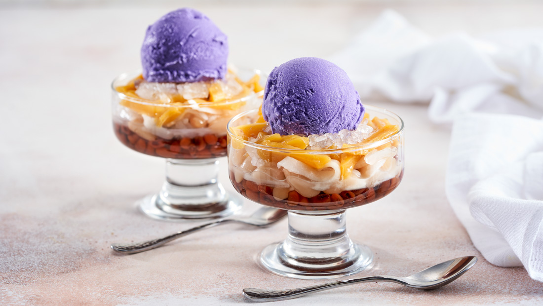 Two clear glass bowls with stem bases filled with Filipino Ice Sundae with a spoon beside each cup.