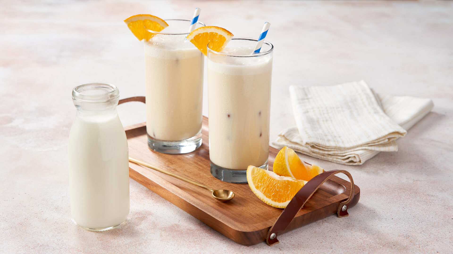  Two glasses of smoothies with orange garnishes and a side of milk 