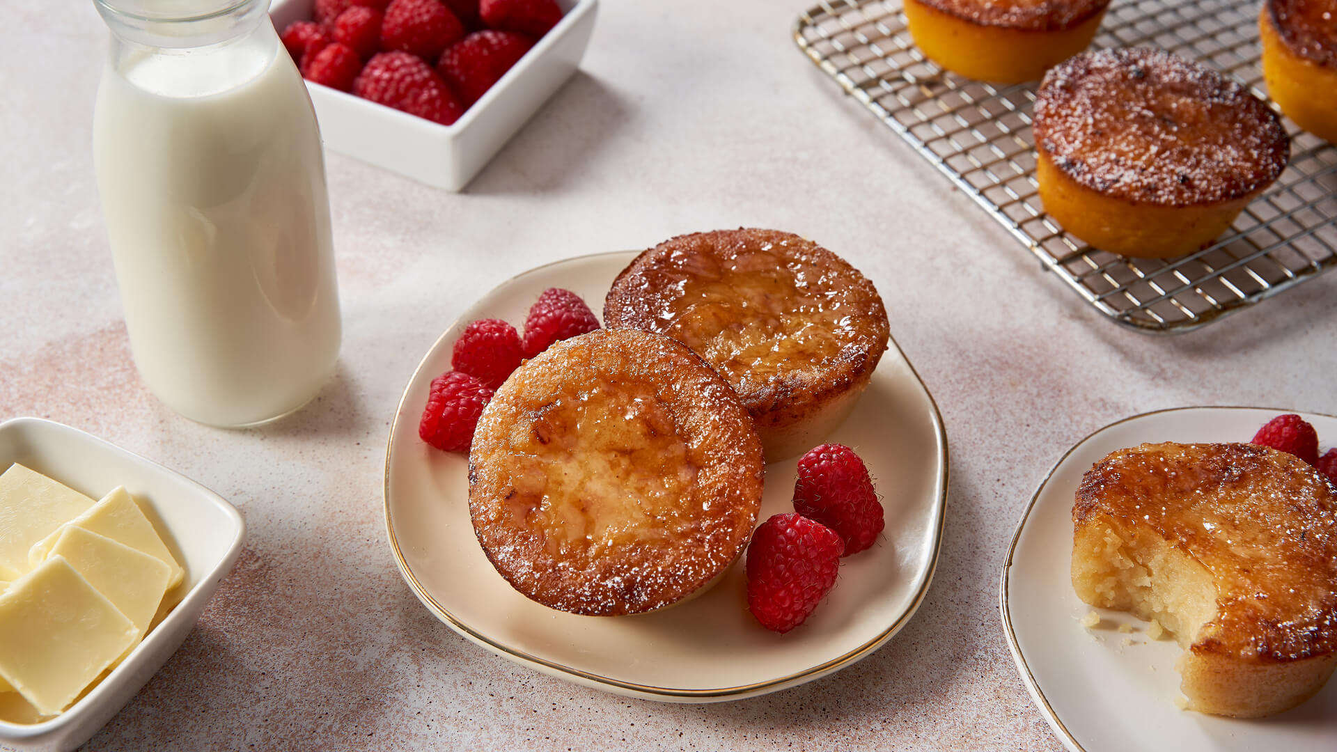 Milk tarts with powdered sugar, raspberries, and a glass of milk and ramekin of butter