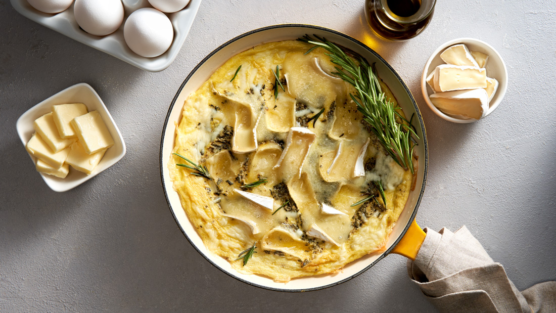 A large pot filled with Rosemary and Brie Frittata garnished with a sprig of rosemary on a white countertop